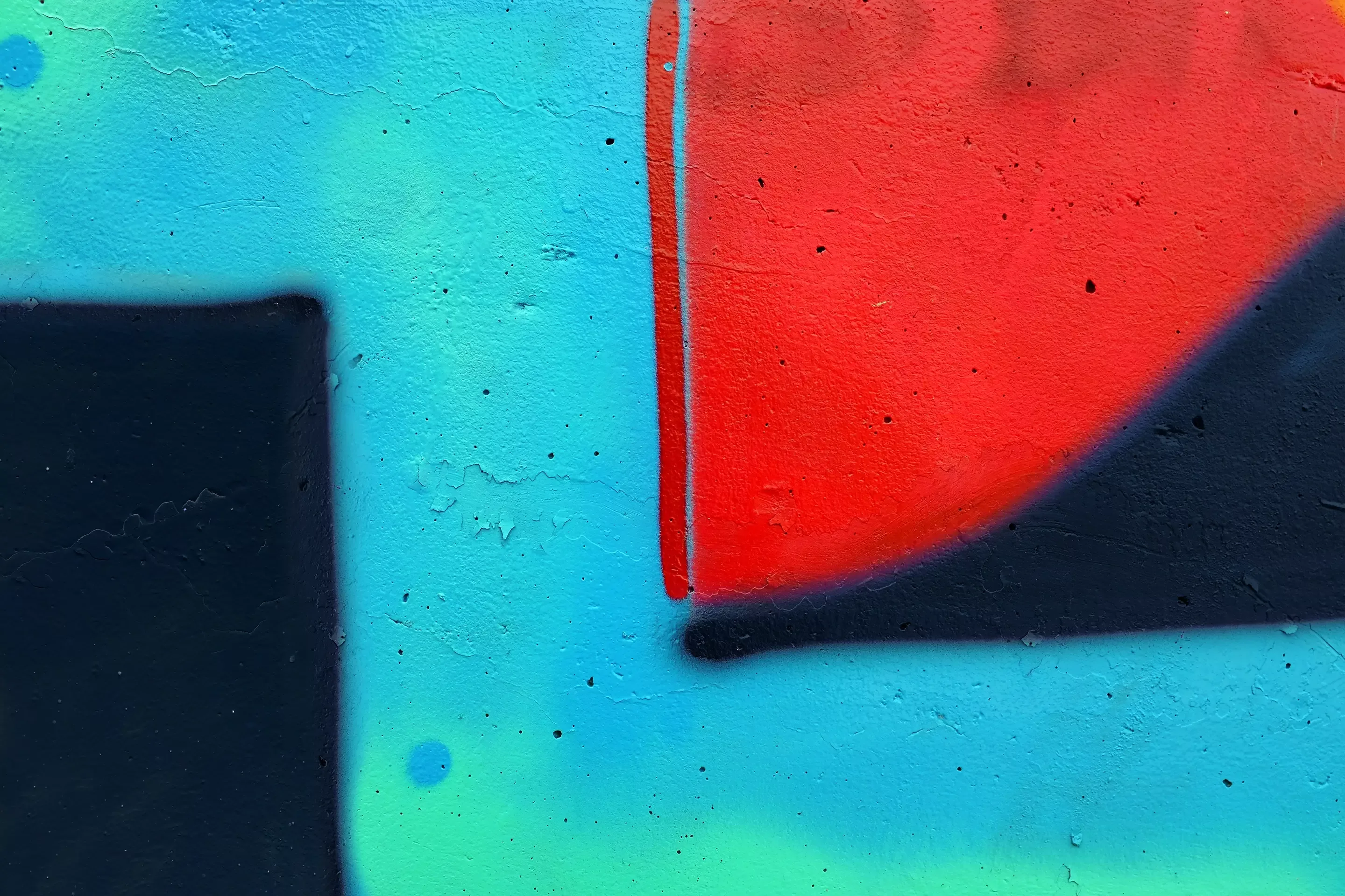 Nahaufnahme eines bunten Graffiti auf einer strukturierten Wand. Auffällige rote und schwarze Formen vor blauem Hintergrund, die eine abstrakte und urbane Atmosphäre vermitteln.